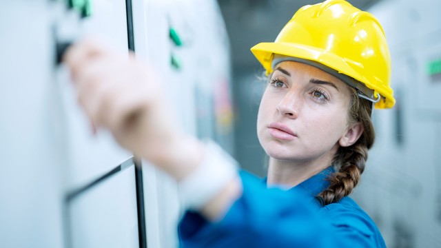 Frau mit gelbem Helm zeichnet etwas an eine Wand