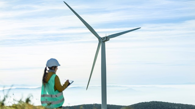 Frau in Warnweste vor einem Windkraftanlage