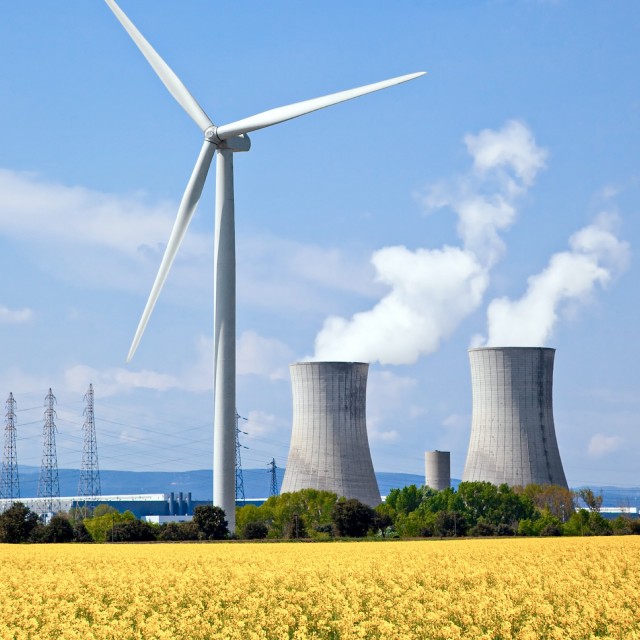 Windrad mit Rapsfeld im Vordergrund und Atomkraftwerk im Hintergrund