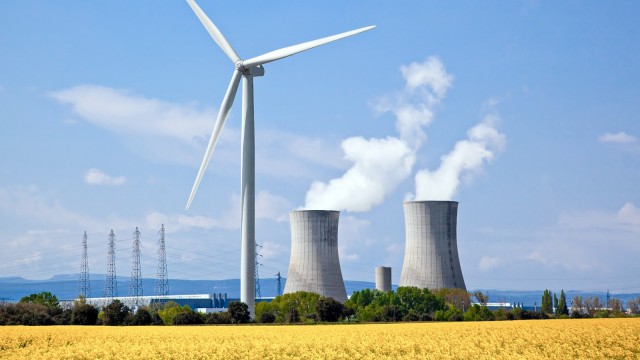 Windrad mit Rapsfeld im Vordergrund und Atomkraftwerk im Hintergrund