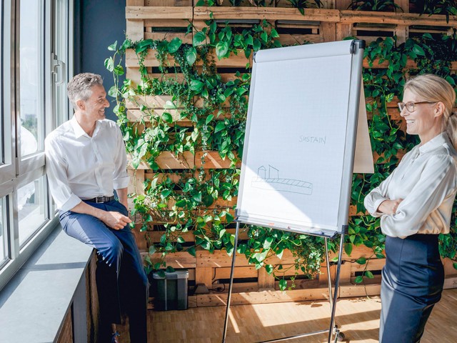 Man and woman next to a flipchart in front of a green office wall 