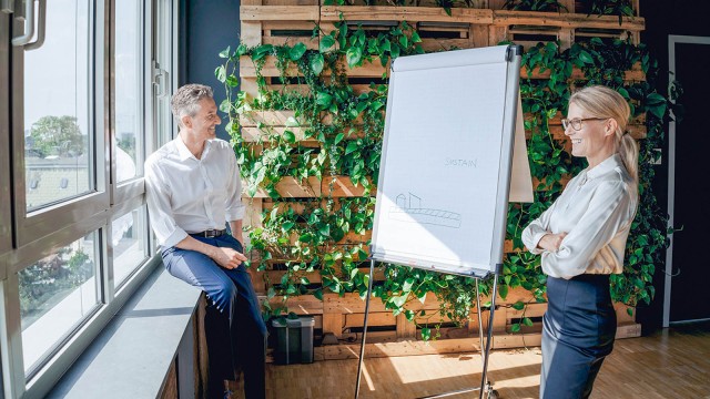 Mann und Frau neben einem Flipchart vor einer begrünter Bürowand 