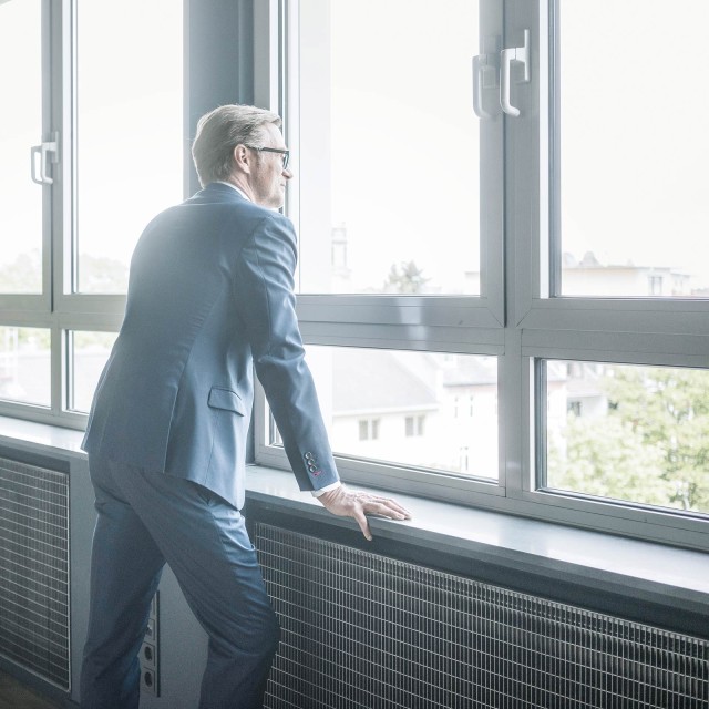 Man in front of green wall looks out the window 