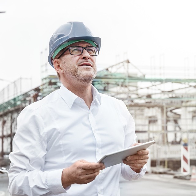 Mann mit Helm und Tablet auf Baustelle 