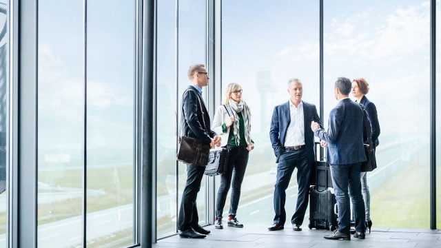 Geschäftsreisende stehen zusammen vor Glasfront und tauschen sich aus