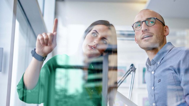 Geschäftsfrau zeigt Geschäftsmann etwas durch die Fensterscheibe