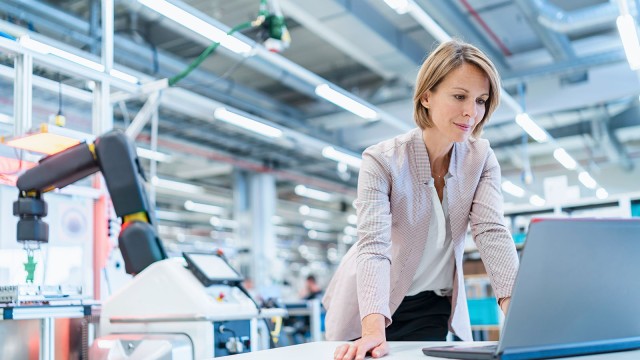 Geschäftsfrau steht in moderner Fabrikhalle am Laptop