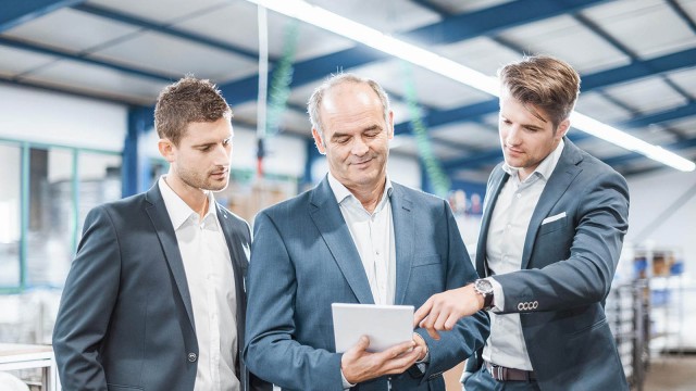 Drei Männer im Anzug in Fabrikhalle 