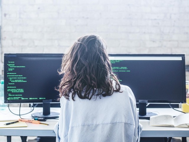 Rückansicht einer weiblichen Hackerin vor Bildschirmen mit Codierung