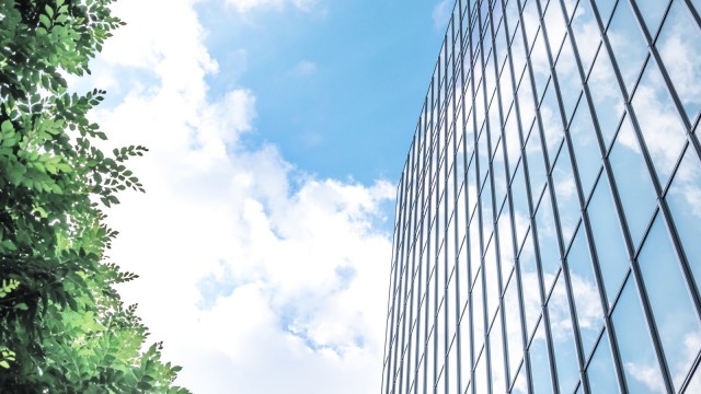 Blauer Himmel zwischen Glasgebäude und grünen Blättern