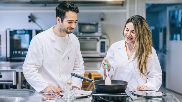 Zwei Personen mit Laborkittel braten Fleisch an