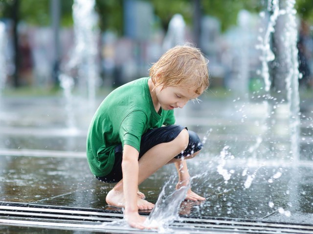 Kind spielt am Brunnen mit Wasser