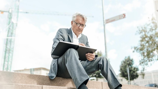 Geschäftsmann auf der Treppe sitzend mit Notizbuch vor dem Baukran 