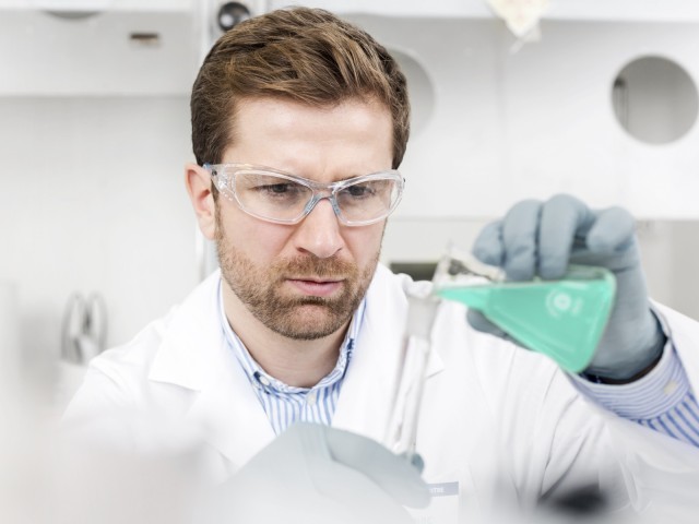 Mann im Labor mit gr&uuml;ner Fl&uuml;ssigkeit und Schutzbrille