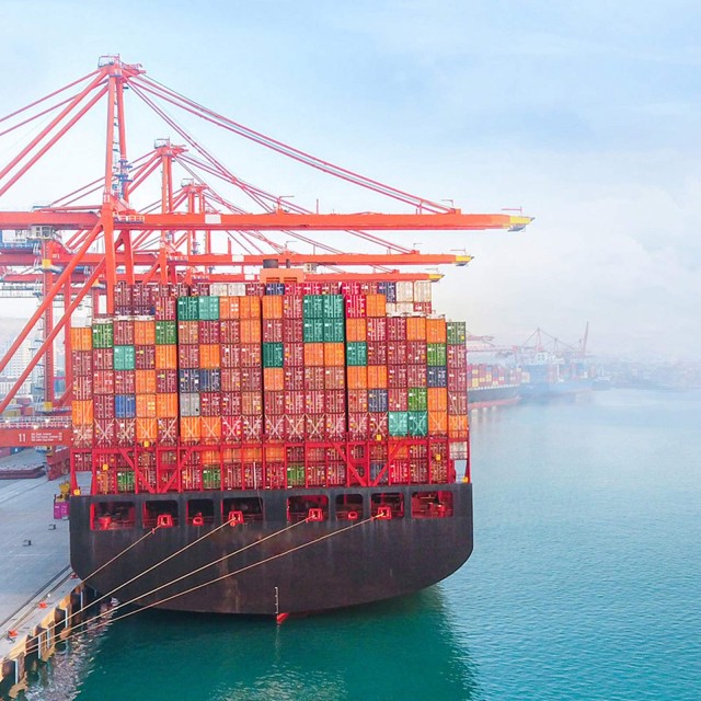 Containerschiff liegt im Hafen mit Kränen im Hintergrund