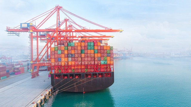 Containerschiff liegt im Hafen mit Kränen im Hintergrund